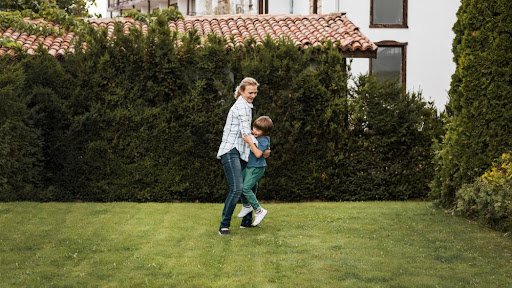 lady and kid playing at home lawn covered with shade trees