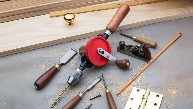 Manual hand drill on wooden workbench with tools